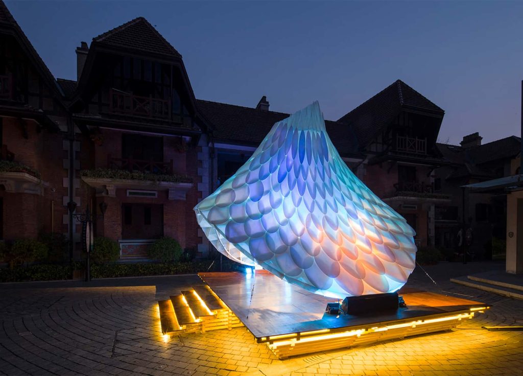 ResoNet Pavilion is commissioned by Sinan Mansions in Shanghai for the celebration of Chinese New Year of the Rooster. The temporary pavilion is made of polypropylene sheets attached with an interactive LED light ResoNet. The Pavilion illuminates the public realm in response to vibration stimuli and works as a centre stage for outdoor events. Its colour changed due to the peripheral lighting conditions and visitors’ viewing angles. The phoenix feather like patterns symbolise the prosperity and happiness. The project is aiming to explore the boundaries between nature, art and technology, to create emergent physical & ephemeral conditions.