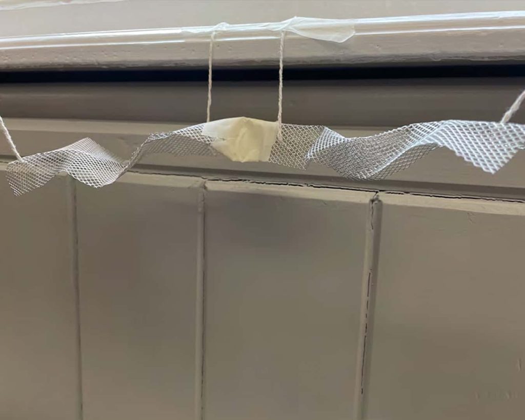 A photograph of wire mesh taped together to take on a snake shape. It is a physical representation of a ceiling insulation.
