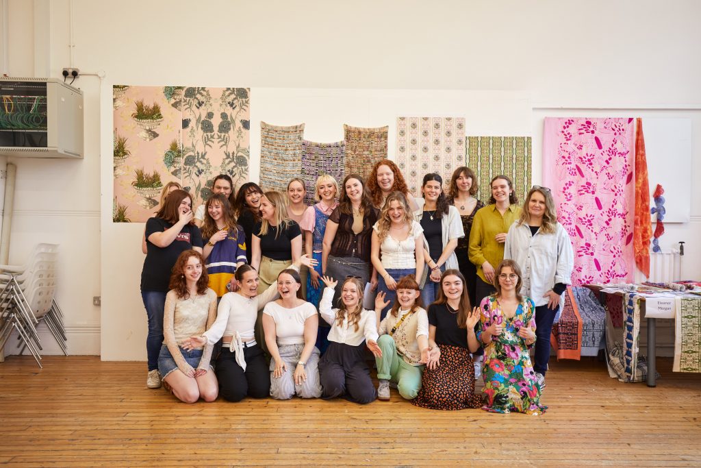 A photo from the Textile Design Industry Awards 2024. The image is of the students in a group smiling and laughing at the camera.