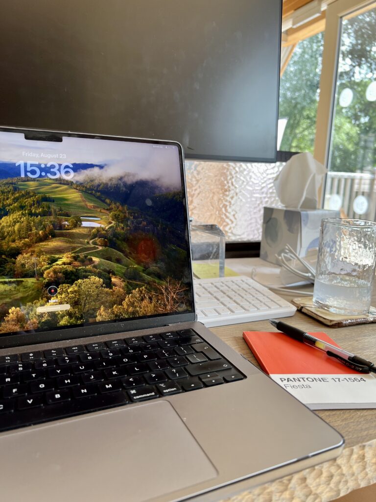 A photo of a laptop screen on a table next to a note pad and pen.