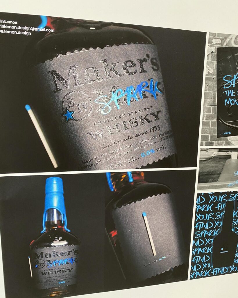 A Maker's Mark whiskey bottle with a dark label featuring the word "SPARK" in blue, handwritten style, and a real matchstick attached. The label emphasizes a creative, spark-inspired theme.