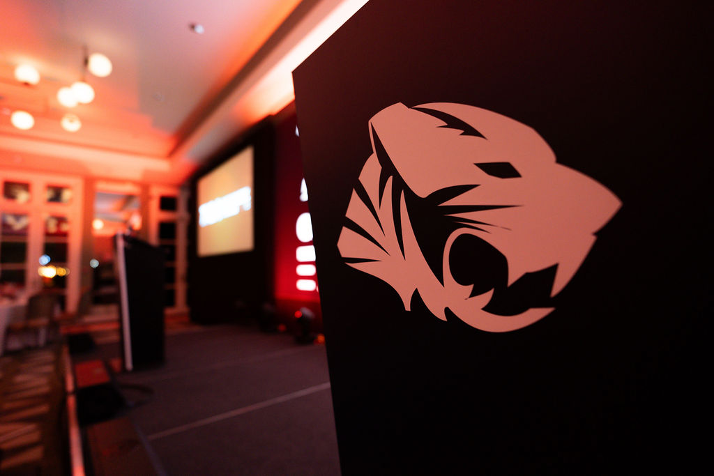 An logo of a stylised tiger printed on a black wall. A stage is out of focus in the background.