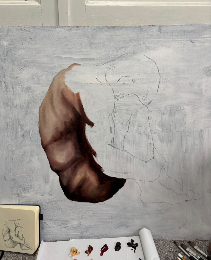 A partially completed painting on canvas shows a figure in a curled, seated position. The torso is painted in browns and creams, while the rest is outlined. A sketchbook with a similar drawing sits next to paint supplies below.